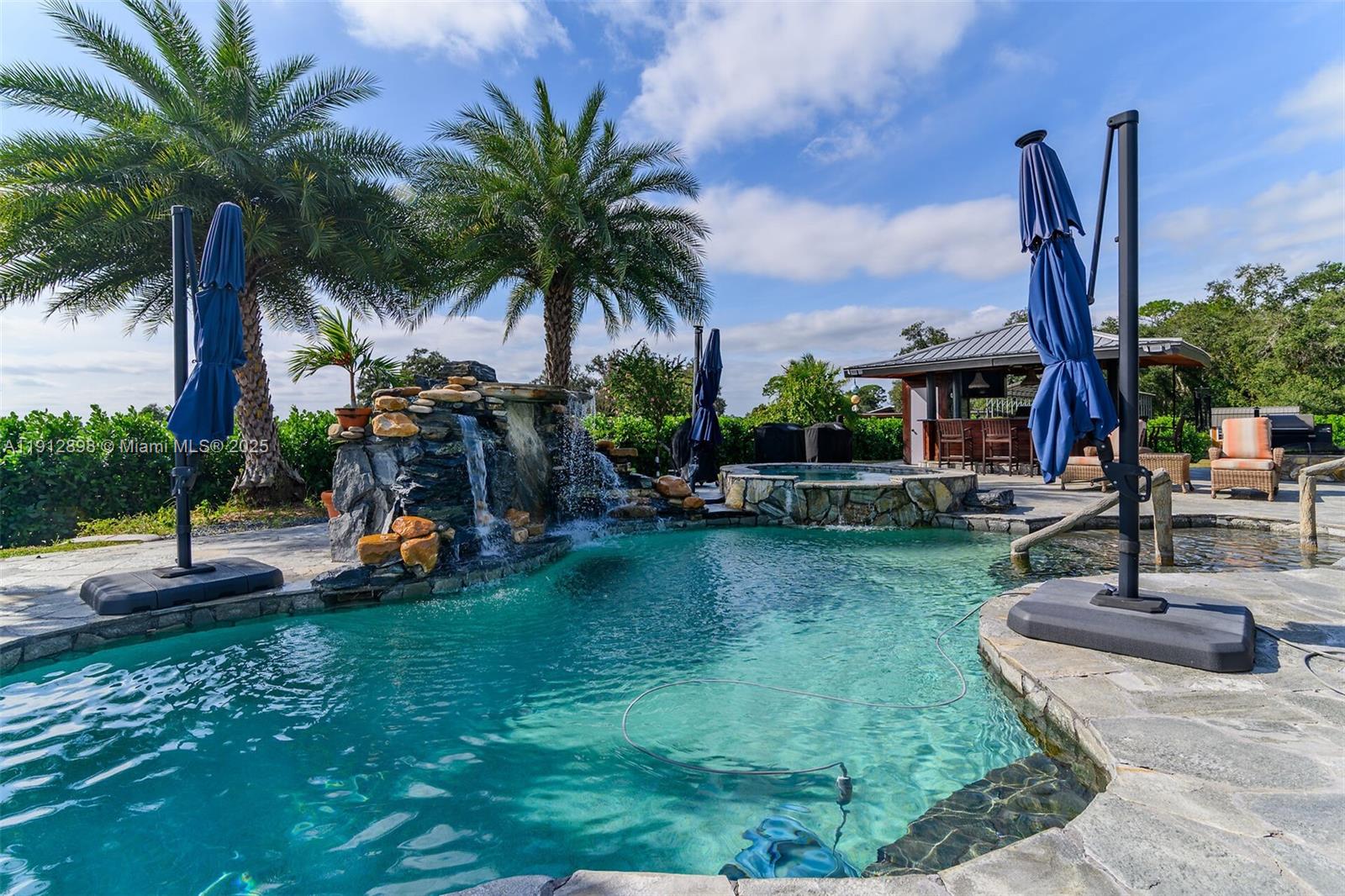 A swimming pool with a rock waterfall and hot tub sits on a stone patio — 5675 County Road 78, La Belle FL 33935, LA BELLE, FL