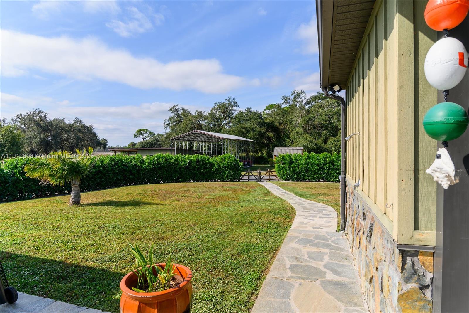 A stone walkway leads across a grassy yard toward a metal carport and hedge — 5675 County Road 78, La Belle FL 33935, LA BELLE, FL
