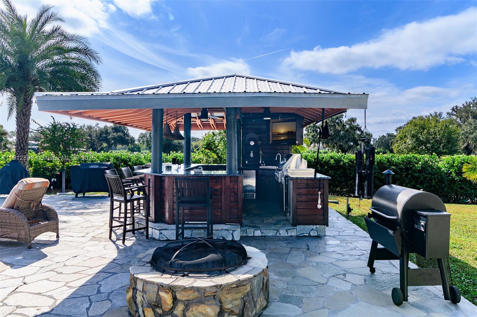 An outdoor kitchen with a bar, grill, and fire pit sits on a stone patio — 5675 County Road 78, La Belle FL 33935, LA BELLE, FL