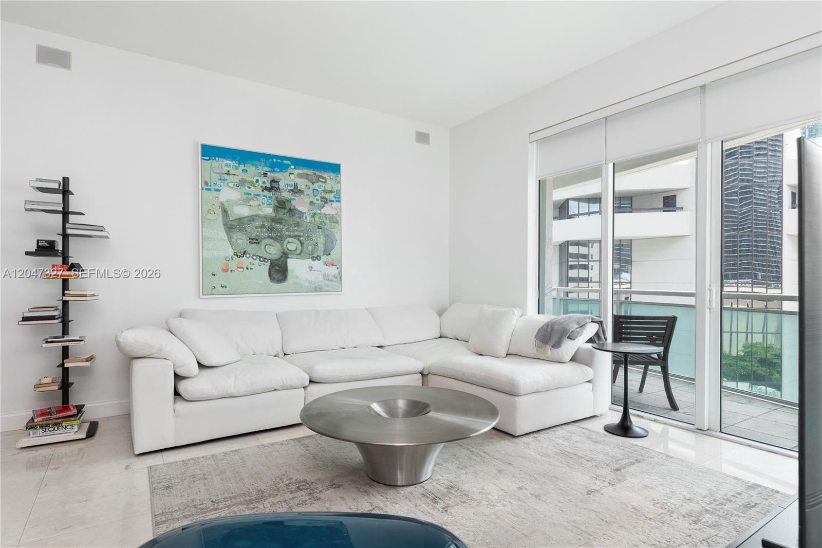 A modern living room features a white sectional sofa, a metal coffee table, and a bookshelf — 951 Brickell Ave # 1011, Miami FL 33131, MIAMI, FL