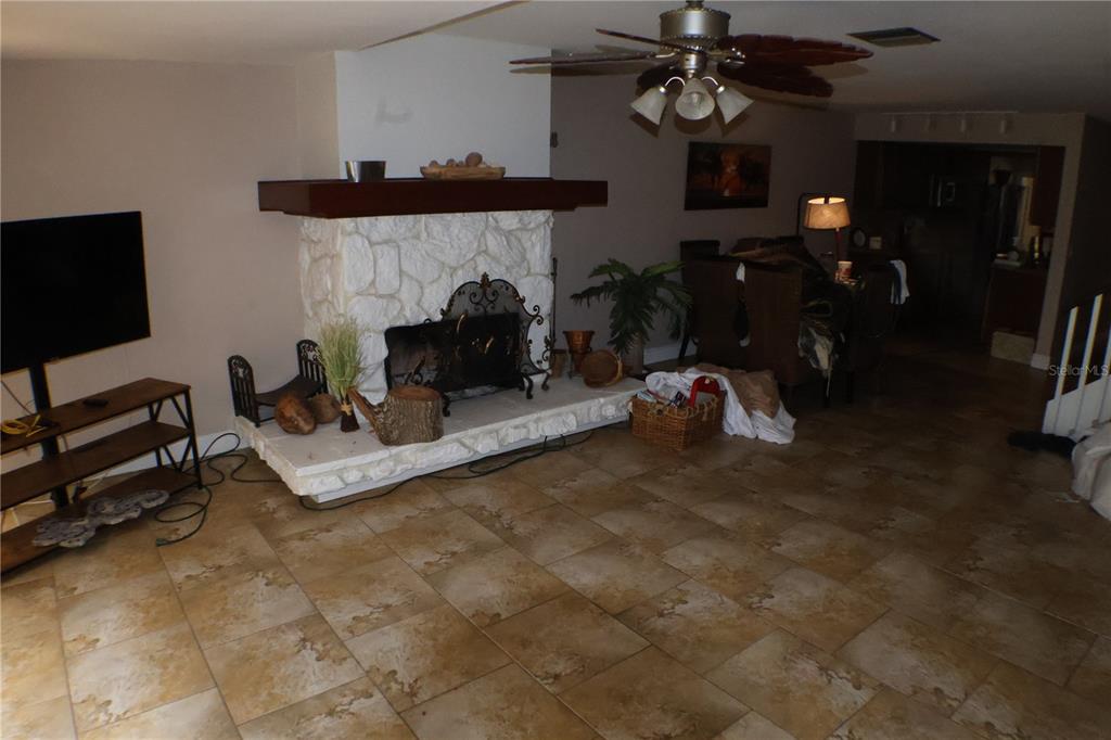 A living room features a white stone fireplace, tile flooring, and a ceiling fan — 3003 FINSTERWALD DRIVE UNIT 3, TITUSVILLE, FL