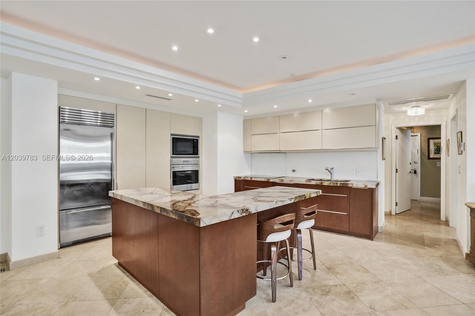 A modern kitchen features a marble-topped island, wood cabinetry, and stainless steel appliances — 9601 Collins Ave # 402, Bal Harbour FL 33154, BAL HARBOUR, FL