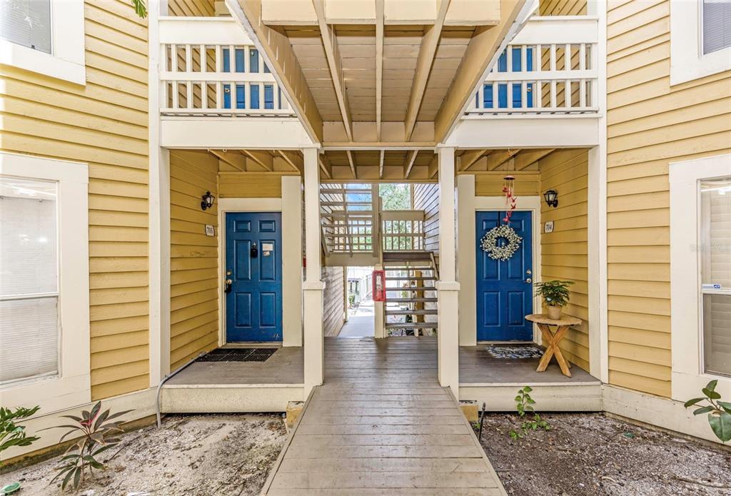 An exterior view of two blue apartment doors connected by a wooden walkway and stairs — 115 112TH AVENUE NE UNIT 703, ST PETERSBURG, FL
