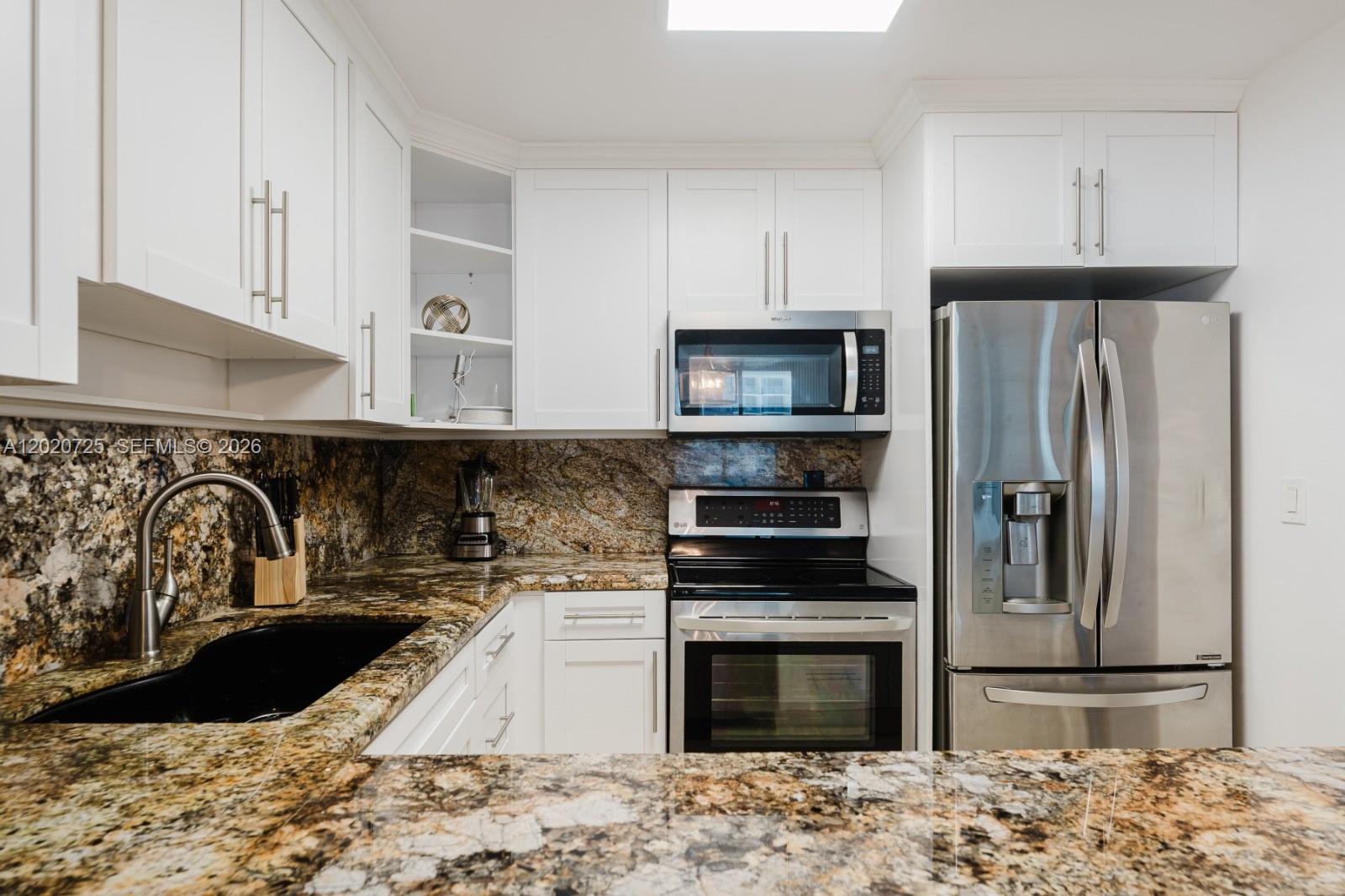 A kitchen features white cabinets, stainless steel appliances, and dark granite countertops — 2301 Collins Ave # 804, Miami Beach FL 33139, MIAMI BEACH, FL
