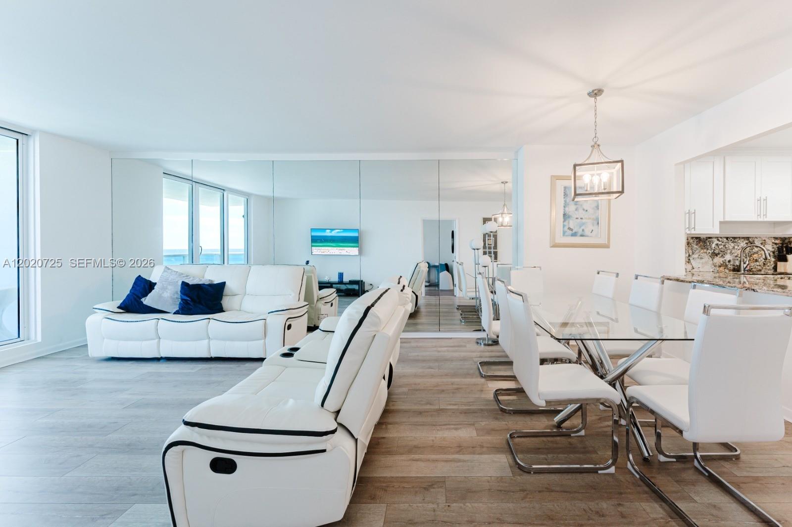 A living and dining area features white leather furniture, a glass table, and mirrored walls — 2301 Collins Ave # 804, Miami Beach FL 33139, MIAMI BEACH, FL