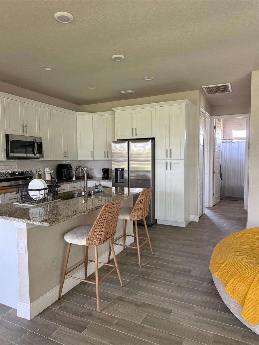 A kitchen features white cabinets, granite countertops, stainless steel appliances, and two woven bar stools — 368 NEIGHBORLY RD, La Belle FL 33935, LA BELLE, FL