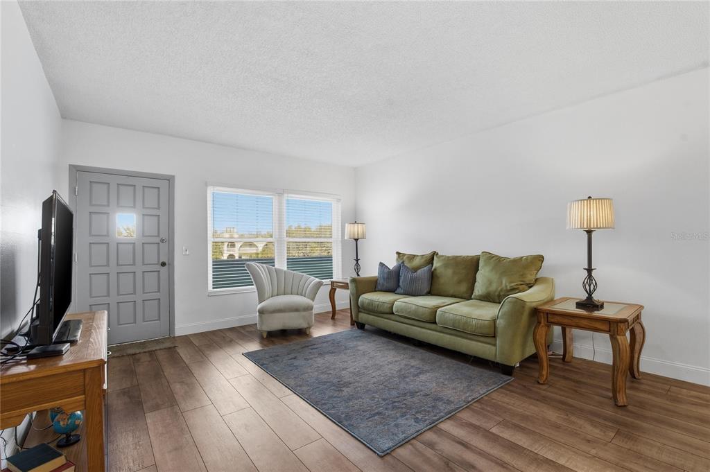 A living room features wood-look flooring, a green sofa, a grey armchair, and a front door — 2257 WORLD PARKWAY BOULEVARD W UNIT 61, CLEARWATER, FL