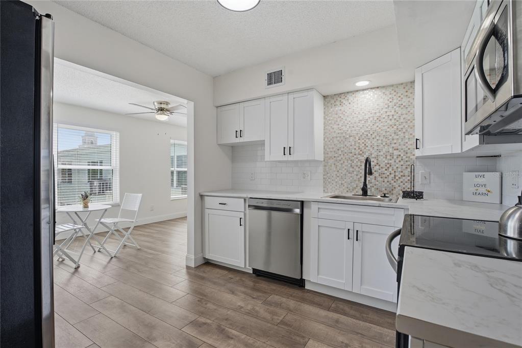 A kitchen with white cabinets, stainless steel appliances, and a mosaic tile backsplash — 2257 WORLD PARKWAY BOULEVARD W UNIT 61, CLEARWATER, FL