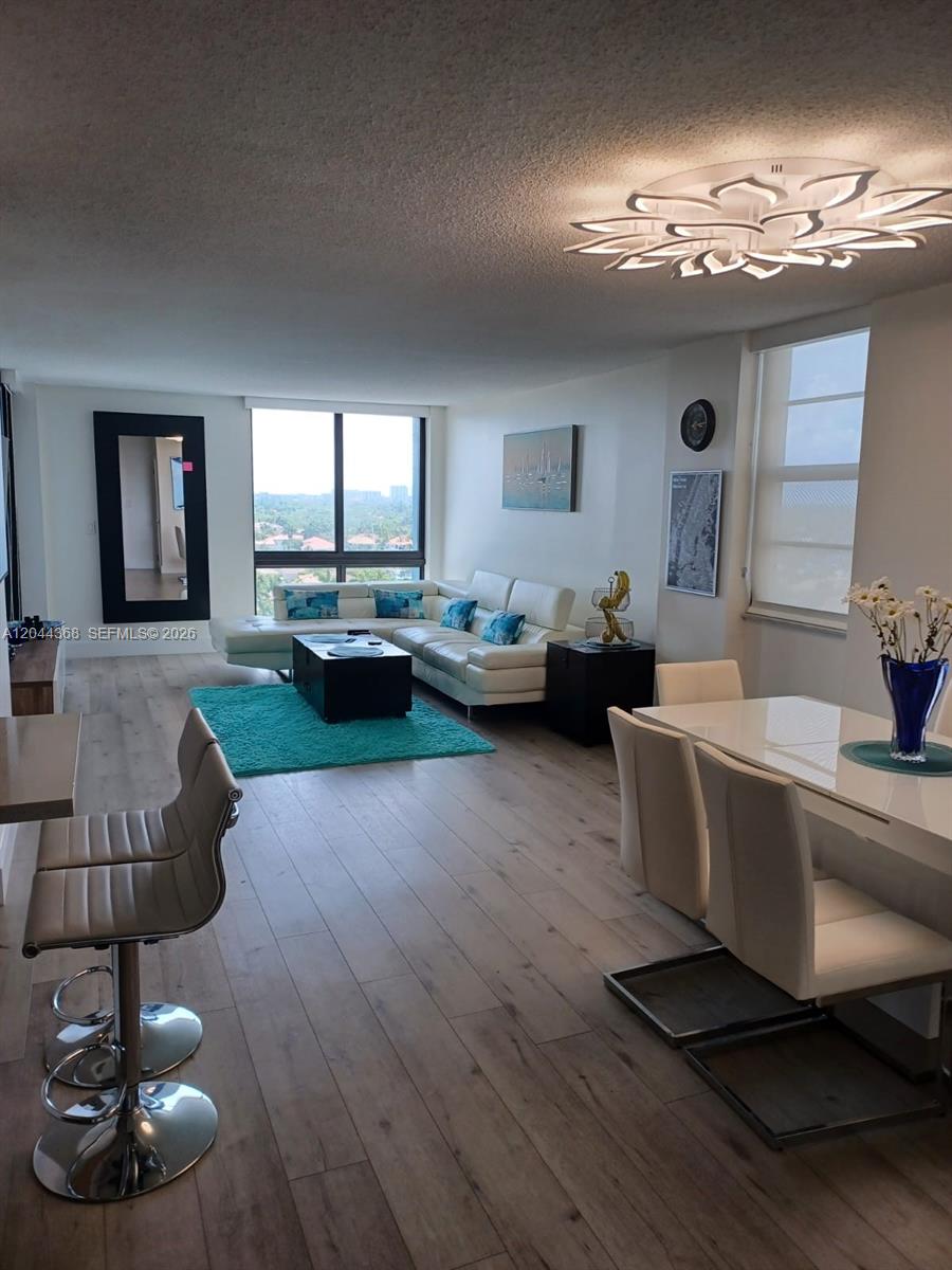 An open-concept living and dining area features light wood floors, white furniture, and large windows — 1600 S Ocean Dr # 12F, Hollywood FL 33019, HOLLYWOOD, FL