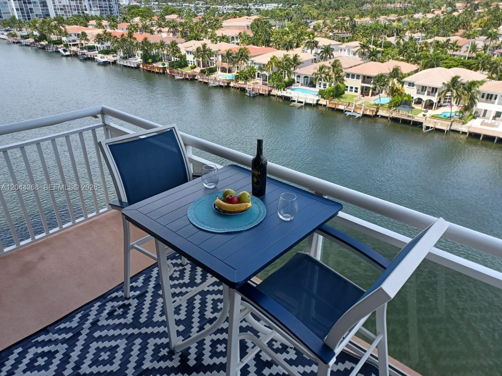 A balcony with a small table, two chairs, and a view of a canal and houses — 1600 S Ocean Dr # 12F, Hollywood FL 33019, HOLLYWOOD, FL
