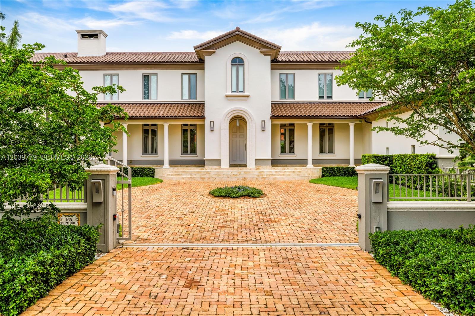 A two-story white stucco house features a tiled roof, arched entryway, and brick driveway — 165 Paloma Dr, Coral Gables FL 33143, CORAL GABLES, FL