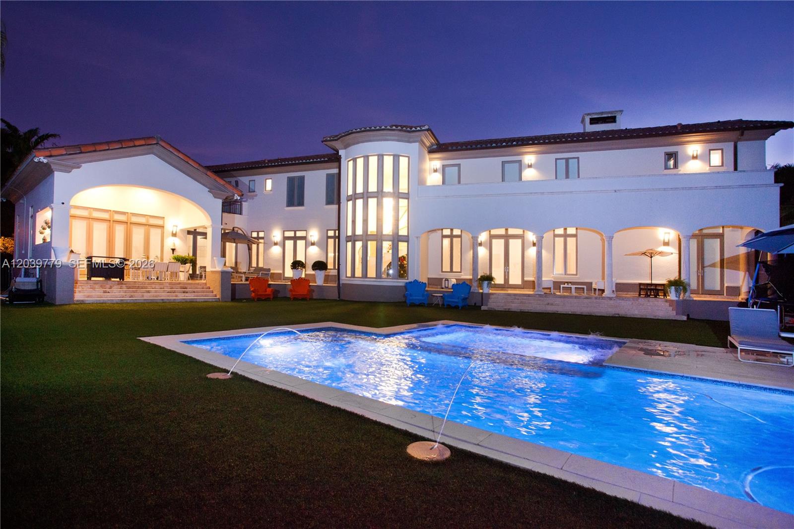 A large two-story house with a swimming pool and fountain jets at twilight — 165 Paloma Dr, Coral Gables FL 33143, CORAL GABLES, FL