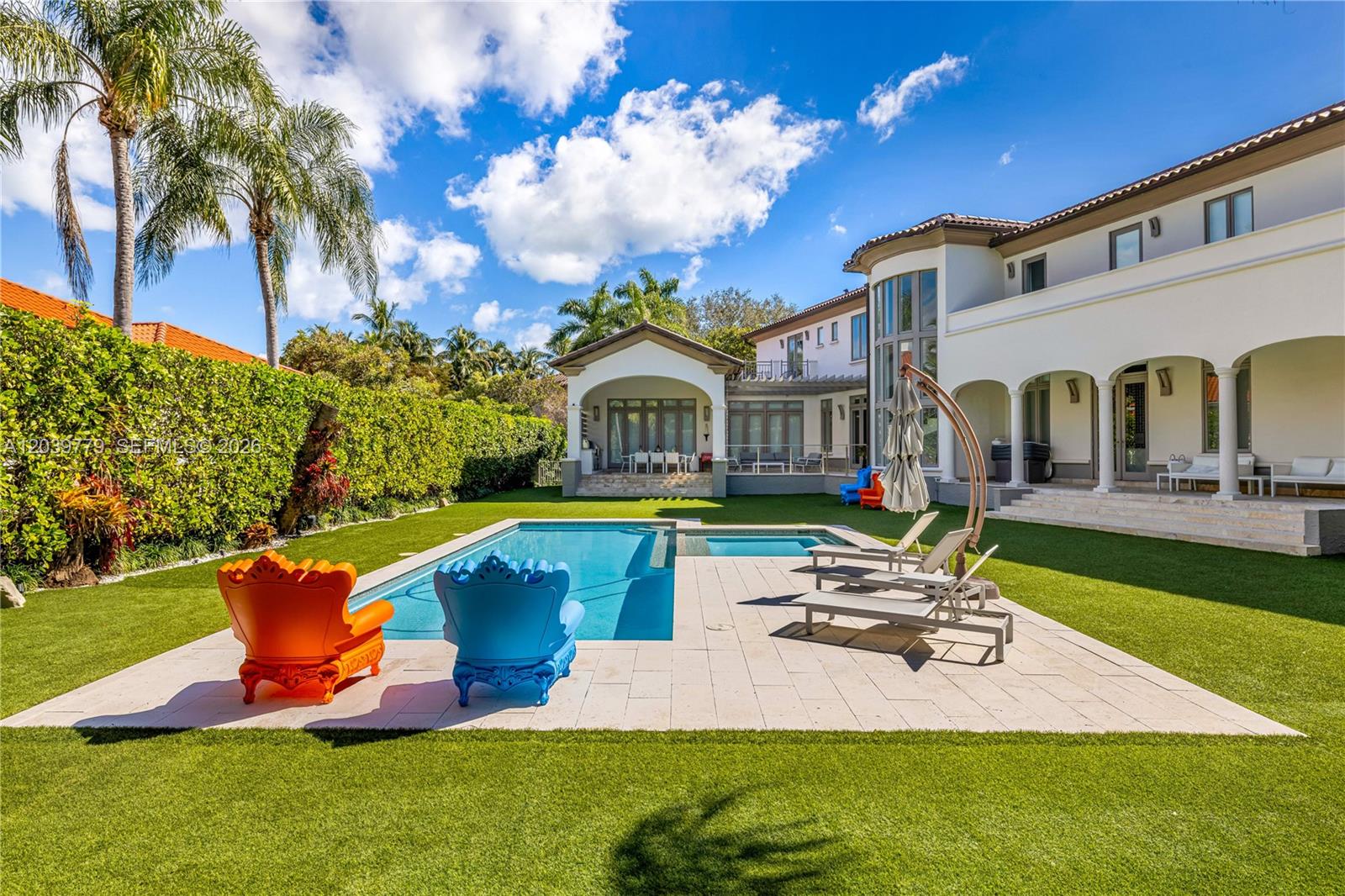 A backyard features a swimming pool, lounge chairs, colorful armchairs, and a large white house — 165 Paloma Dr, Coral Gables FL 33143, CORAL GABLES, FL