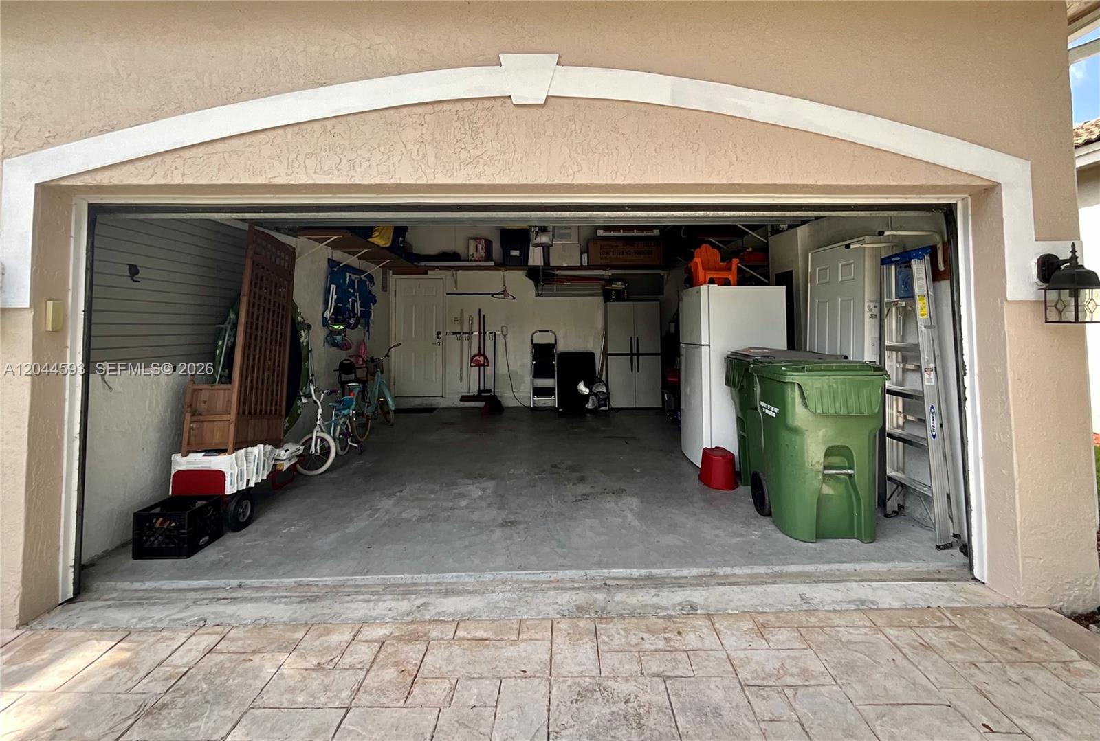 A two-car garage with a concrete floor, storage items, bicycles, and a white refrigerator — 2335 SE 4th Pl, Homestead FL 33033, HOMESTEAD, FL