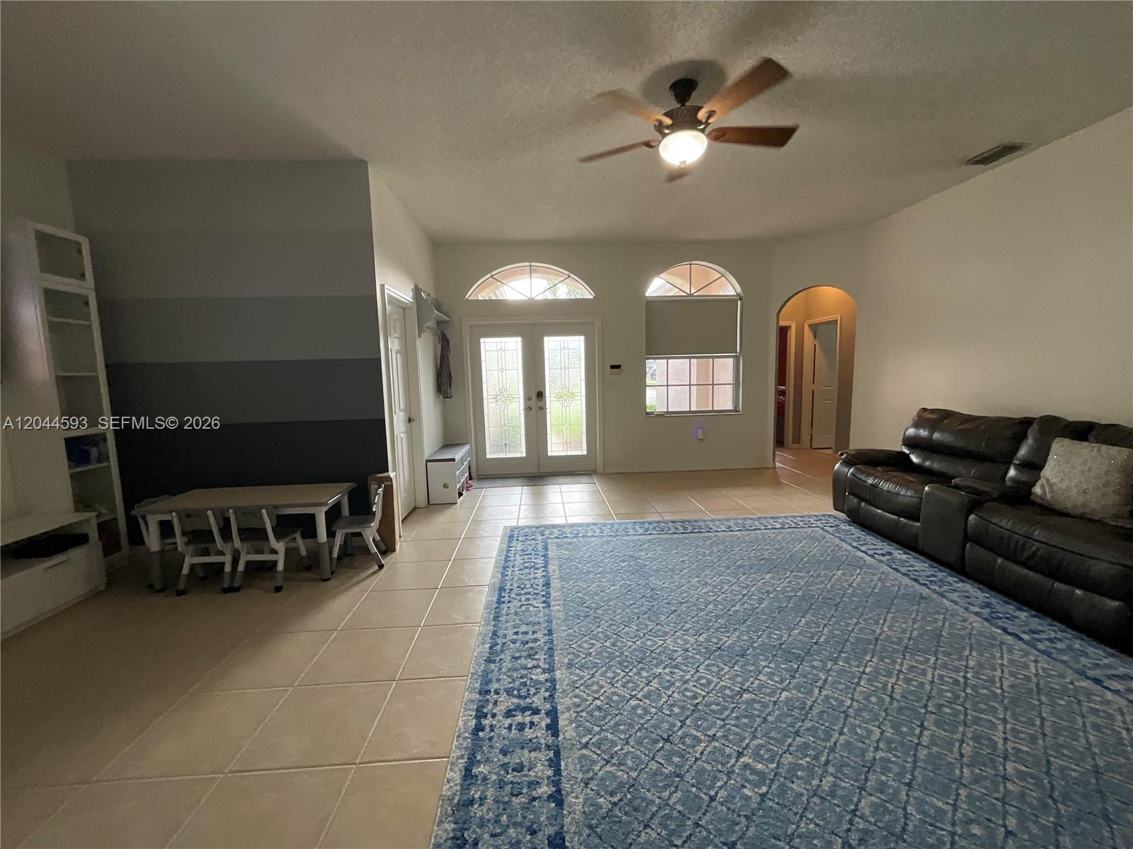 A living room features tile flooring, a large blue rug, and a ceiling fan — 2335 SE 4th Pl, Homestead FL 33033, HOMESTEAD, FL