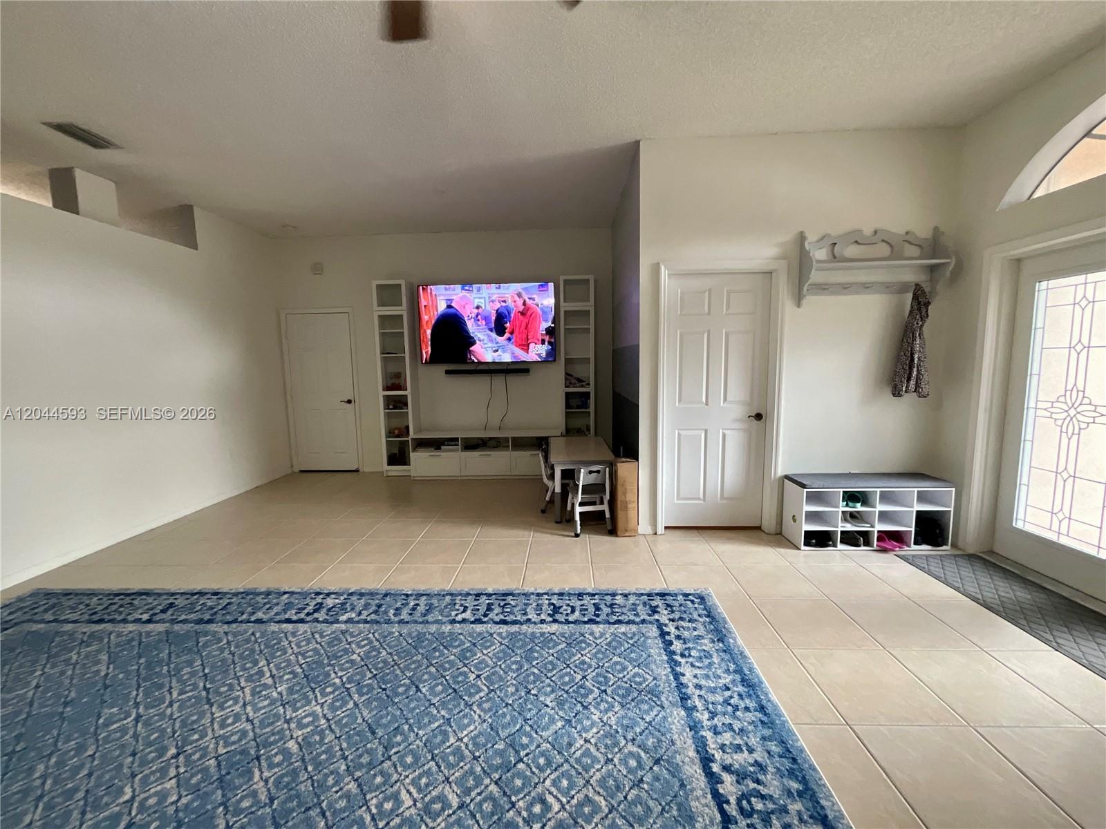 A living room features tile flooring, a large blue rug, and a wall-mounted television — 2335 SE 4th Pl, Homestead FL 33033, HOMESTEAD, FL