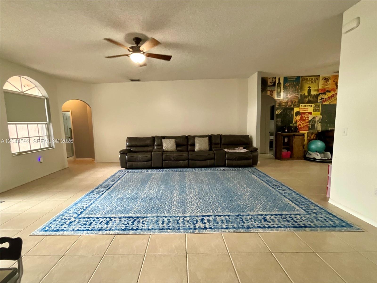A living room features a large blue area rug, a dark leather sofa, and tile flooring — 2335 SE 4th Pl, Homestead FL 33033, HOMESTEAD, FL