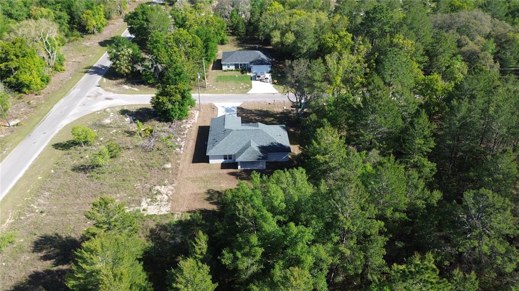 An aerial view shows a single-story house with a gray roof surrounded by wooded land — 102 MALAUKA TRAIL, OCKLAWAHA, FL