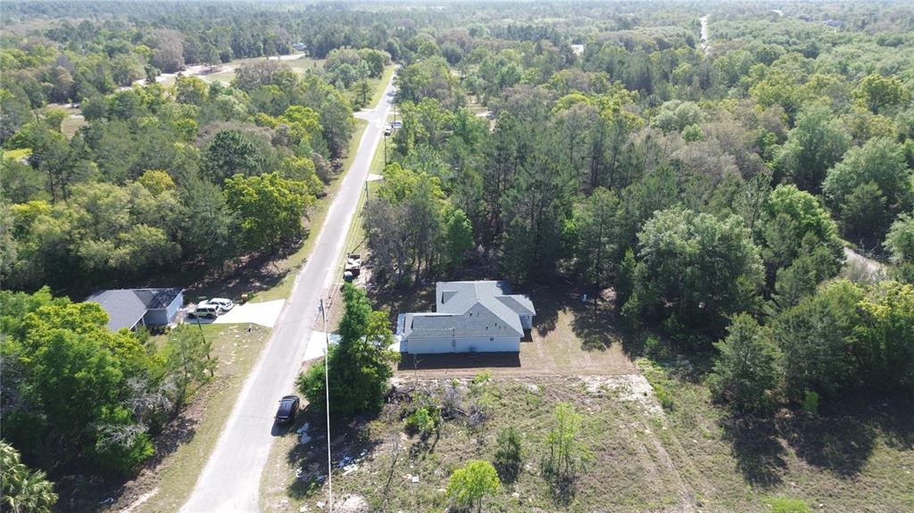 An aerial view shows a single-story house surrounded by dense trees and a paved road — 102 MALAUKA TRAIL, OCKLAWAHA, FL