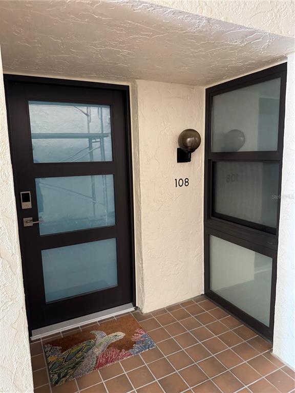 A dark brown front door with frosted glass panels sits next to a matching side window — 2089 GULF OF MEXICO DRIVE UNIT G1-108, LONGBOAT KEY, FL