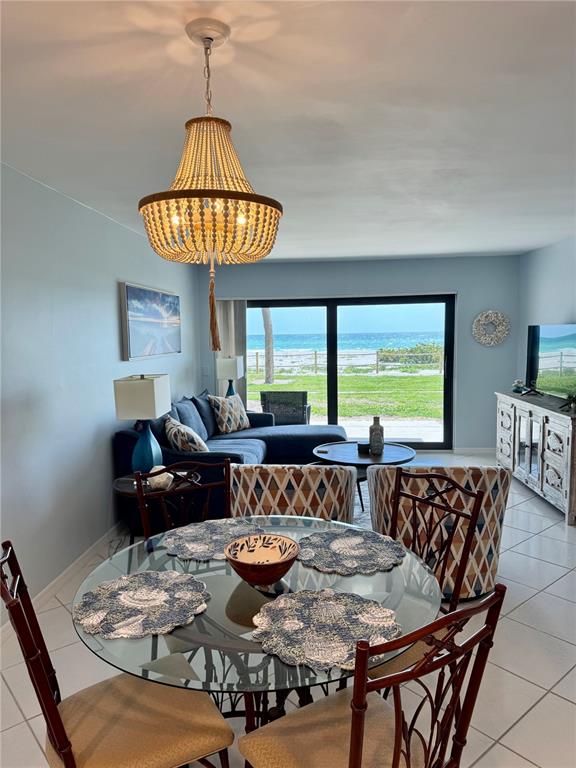 A dining area with a glass table and beaded chandelier overlooks a beach and ocean — 2089 GULF OF MEXICO DRIVE UNIT G1-108, LONGBOAT KEY, FL