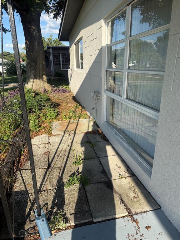 A concrete patio area sits beside the exterior wall of a house with large windows — 5232 KAPOK DRIVE, NEW PORT RICHEY, FL