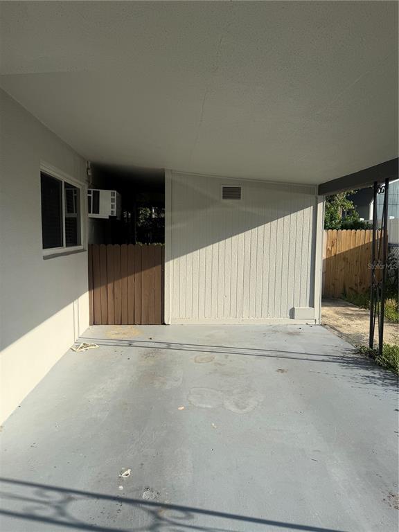 A covered concrete carport features a white exterior wall and a wooden privacy fence — 5232 KAPOK DRIVE, NEW PORT RICHEY, FL