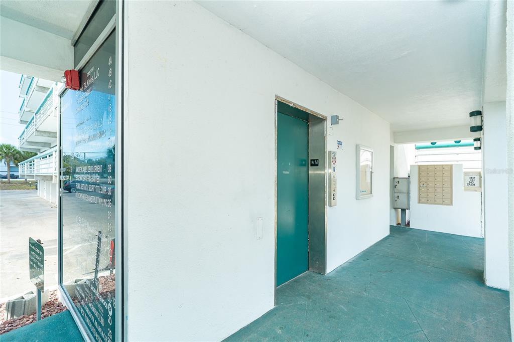 An outdoor hallway features a green elevator door, a directory sign, and a mail station — 1460 S MCCALL ROAD UNIT E3, ENGLEWOOD, FL