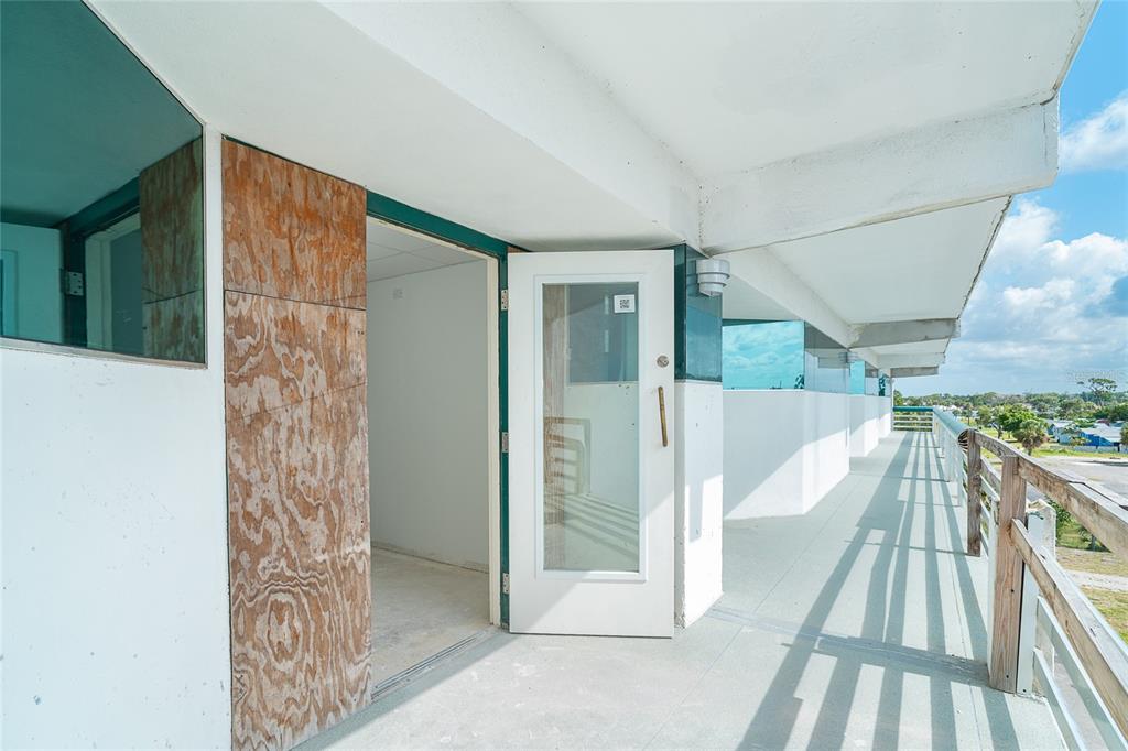 An exterior balcony with a white door leads into an unfinished room with plywood paneling — 1460 S MCCALL ROAD UNIT E3, ENGLEWOOD, FL
