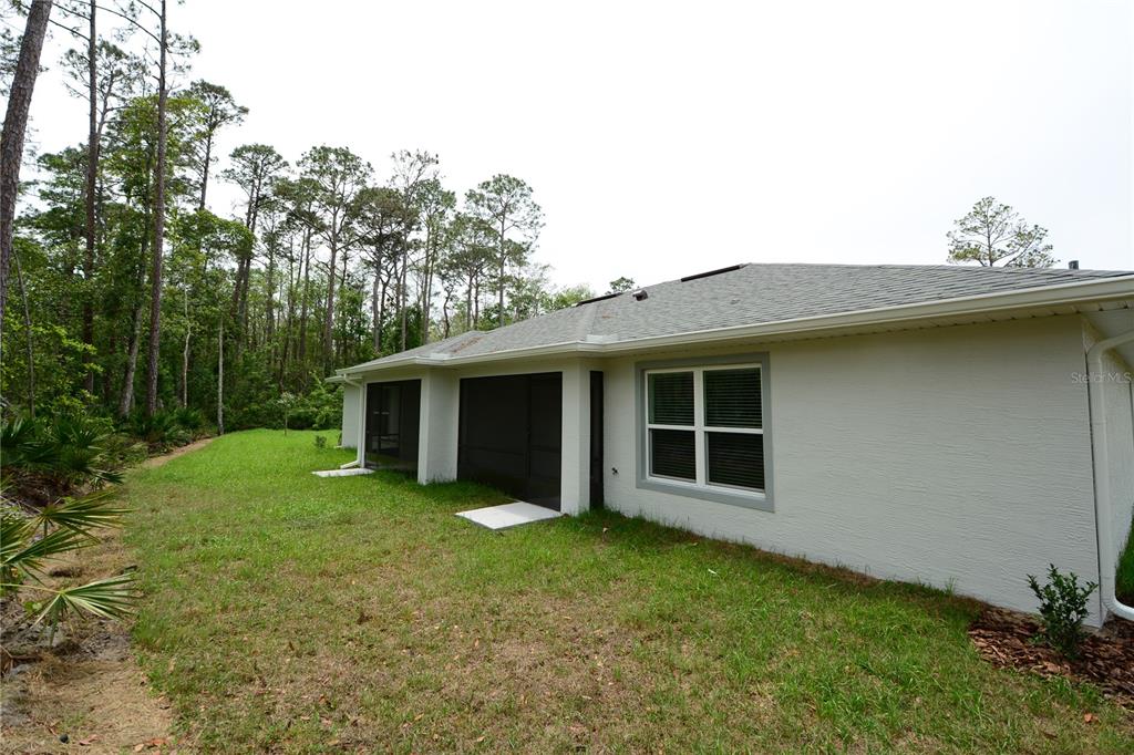 The exterior of a house features a screened-in porch, a window, and a grassy backyard — 31 ZOELLER COURT, PALM COAST, FL