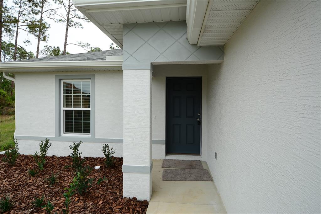 A white stucco house exterior features a dark gray front door and a covered entryway — 31 ZOELLER COURT, PALM COAST, FL