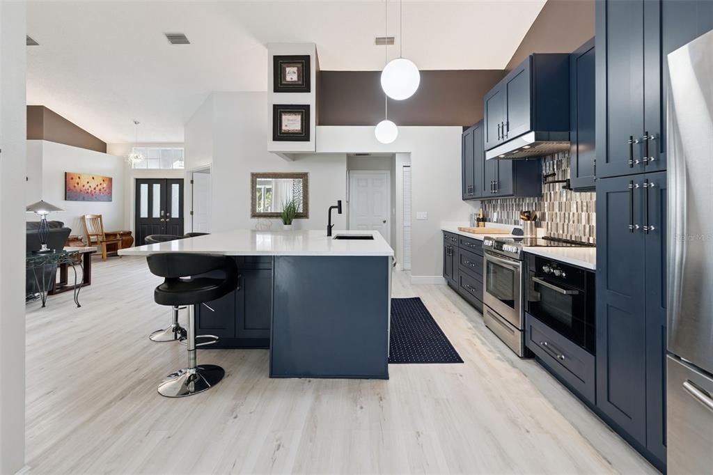 A modern kitchen features dark blue cabinetry, a white island, and light wood-look flooring — 1236 LANSING DRIVE, SPRING HILL, FL