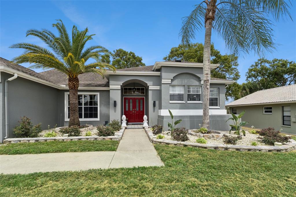 A gray single-story house features a red front door, two palm trees, and stone landscaping — 1236 LANSING DRIVE, SPRING HILL, FL