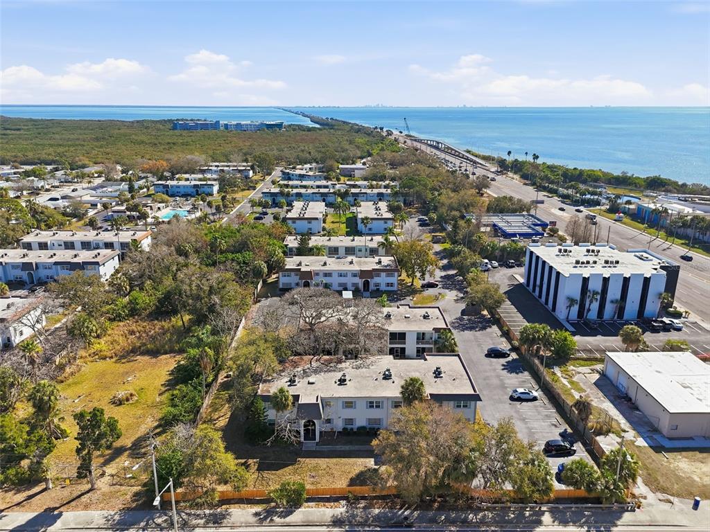 An aerial view shows multiple apartment buildings, parking lots, and a road near the coast — 337 S MCMULLEN BOOTH ROAD UNIT 158, CLEARWATER, FL