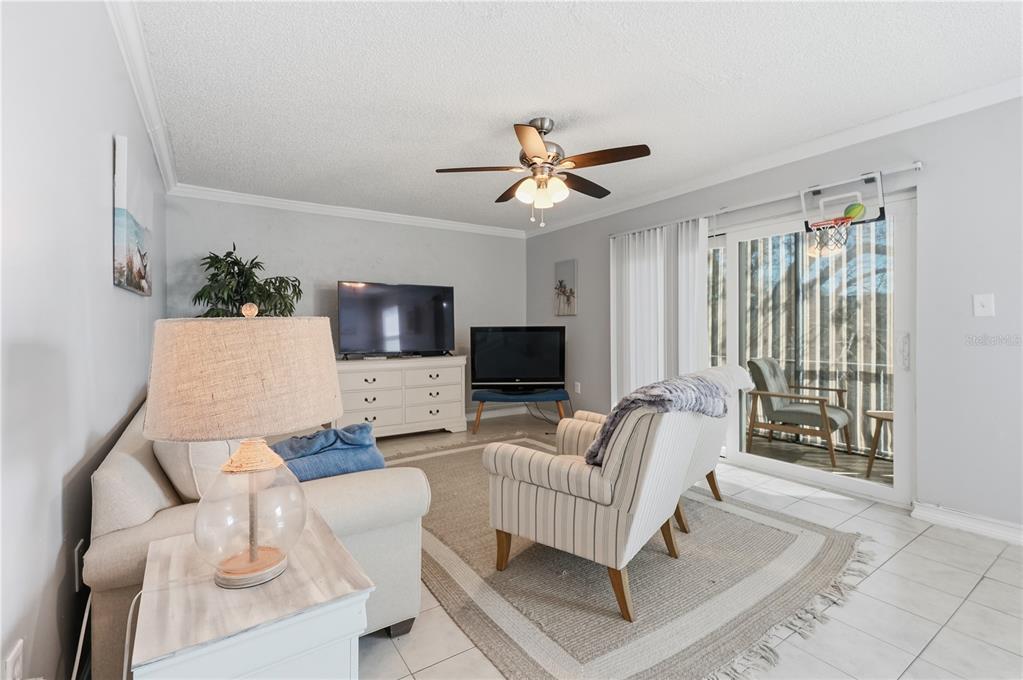 A living room features a sofa, striped armchairs, two televisions, and a sliding glass door — 337 S MCMULLEN BOOTH ROAD UNIT 158, CLEARWATER, FL