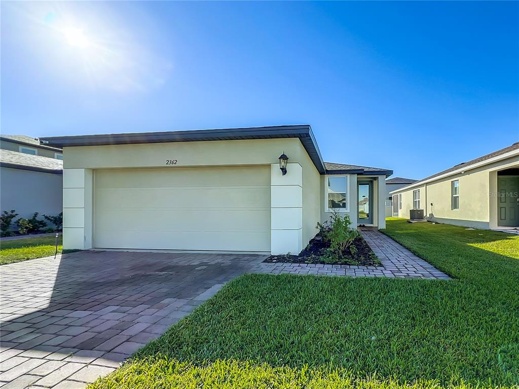 A single-story house with a beige stucco exterior, a two-car garage, and a paved walkway — 2362 BRASSIE COURT, WINTER HAVEN, FL