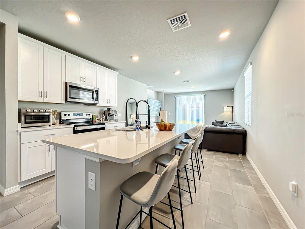A kitchen with white cabinets, a quartz island, and bar seating opens to a living area — 2362 BRASSIE COURT, WINTER HAVEN, FL
