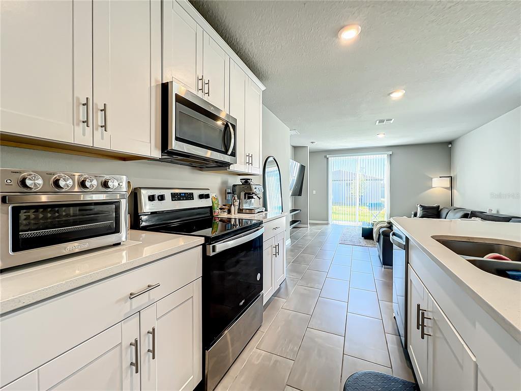 A modern kitchen with white cabinets and stainless steel appliances overlooks an open-concept living area — 2362 BRASSIE COURT, WINTER HAVEN, FL