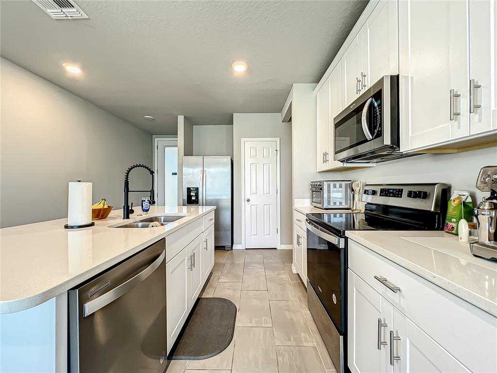 A modern kitchen features white cabinetry, stainless steel appliances, and a large quartz island — 2362 BRASSIE COURT, WINTER HAVEN, FL