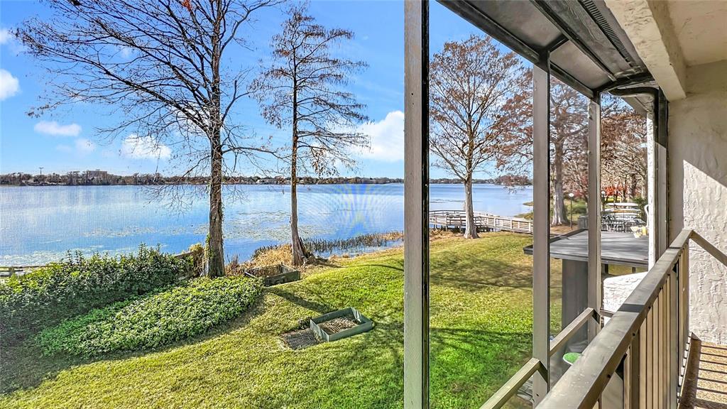 A screened-in balcony overlooks a grassy lawn, trees, and a lake with a wooden dock — 630 KILLARNEY BAY COURT UNIT 3, WINTER PARK, FL