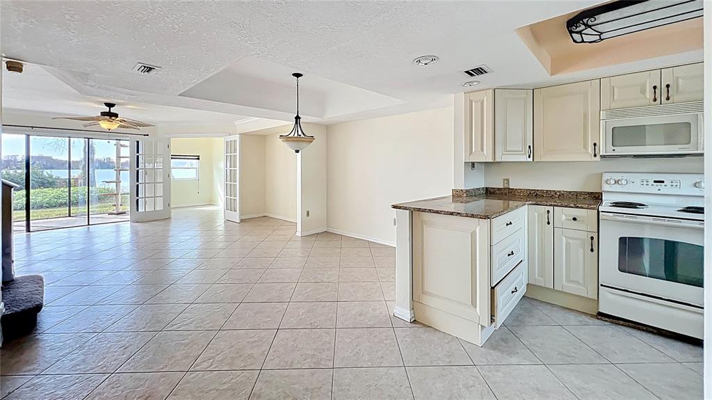 A kitchen with white cabinets and a granite countertop opens into a tiled living area — 630 KILLARNEY BAY COURT UNIT 3, WINTER PARK, FL