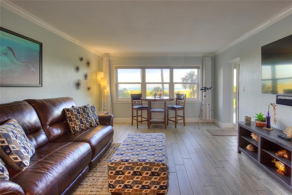 A living room with a leather sofa, patterned ottoman, dining set, and ocean view windows — 1230 GULF BOULEVARD UNIT 304, CLEARWATER, FL