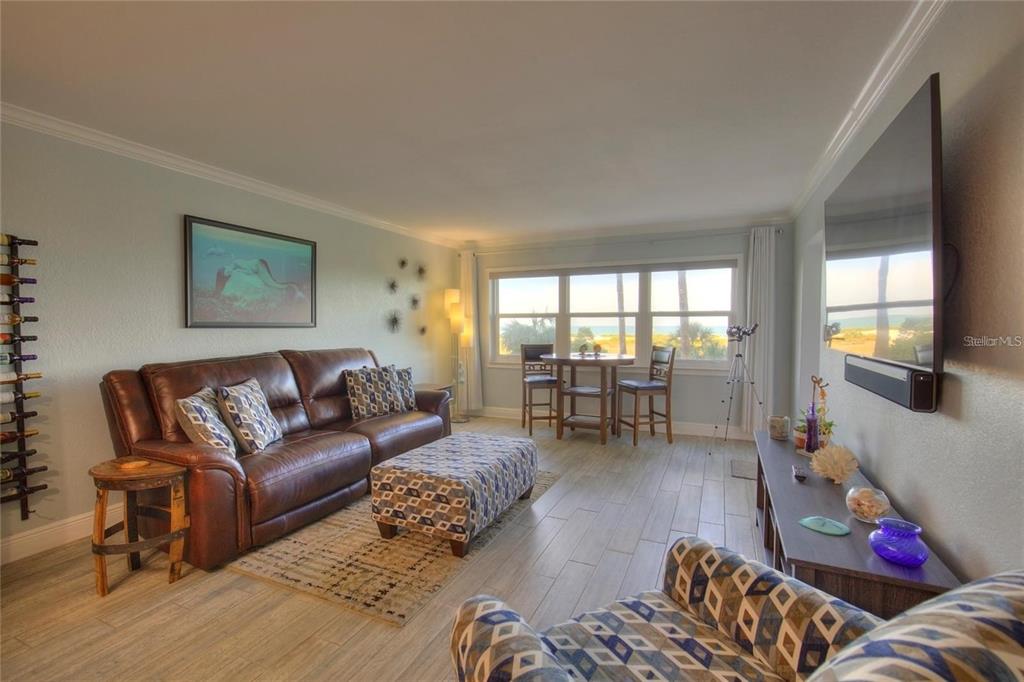 A living room features a leather sofa, patterned ottoman, dining set, and ocean view windows — 1230 GULF BOULEVARD UNIT 304, CLEARWATER, FL