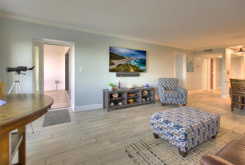 A living room features light tile floors, a wall-mounted television, and a patterned ottoman — 1230 GULF BOULEVARD UNIT 304, CLEARWATER, FL