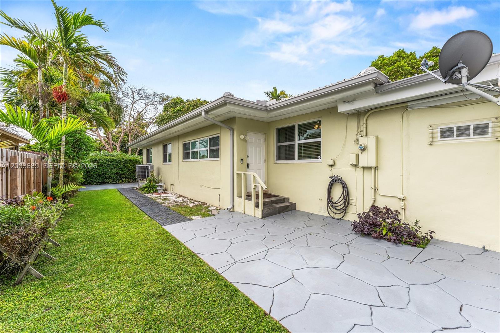 A pale yellow house exterior features a gray stone-patterned patio and a small wooden staircase — 501 Lawn Way, Miami Springs FL 33166, MIAMI SPRINGS, FL