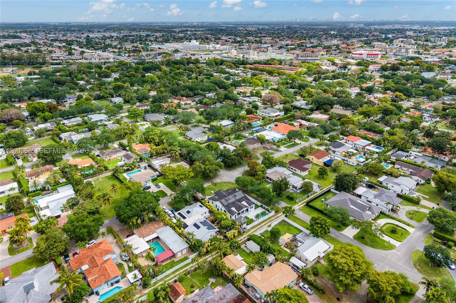 An aerial view shows a suburban neighborhood with houses, swimming pools, and lush green trees — 501 Lawn Way, Miami Springs FL 33166, MIAMI SPRINGS, FL