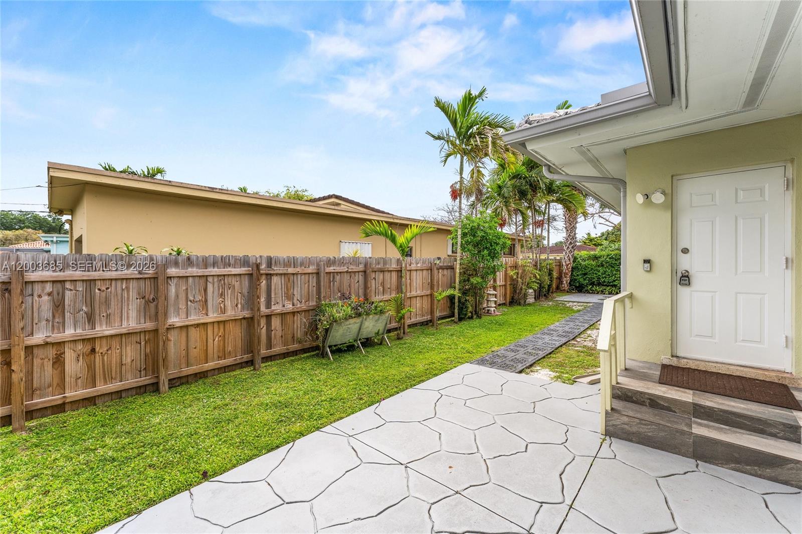 A backyard features a stone-patterned patio, a wooden fence, and a white exterior door — 501 Lawn Way, Miami Springs FL 33166, MIAMI SPRINGS, FL