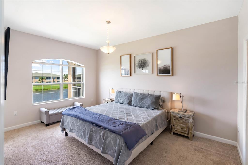 A bedroom features a bed with grey bedding, a window with a water view, and artwork — 6616 7TH AVENUE CIRCLE W UNIT 1311, BRADENTON, FL