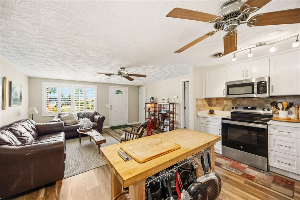 An open-concept living room and kitchen featuring a wooden island, leather sofa, and ceiling fans — 885 E 3RD STREET, ENGLEWOOD, FL