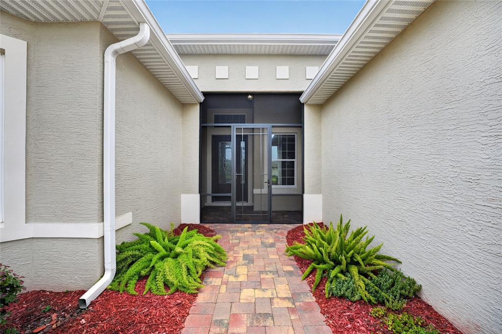 A paved walkway leads to a screened front entryway flanked by two green bushes — 10216 JULIA ISLES AVENUE, OXFORD, FL